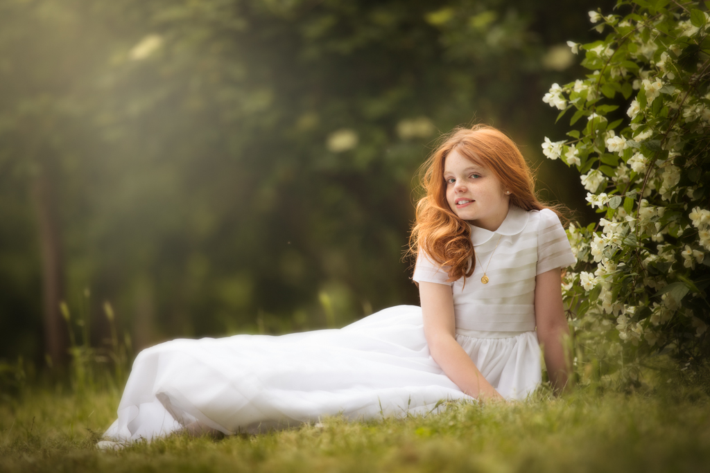 foto de niña pelirroja en vestido blanco el día de su reportaje de primera comunión en exteriores en campo de flores
