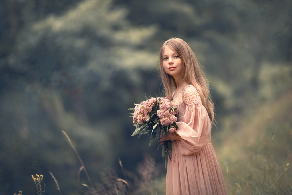 una foto de niña rubia con pelo largo y ramo de flores y vestido rosa en el campo en reportaje fotográfico pre comunión