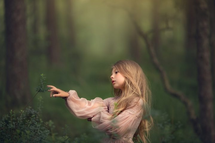 una foto artistica de niña rubia con pelo largo y vestido rosa en un bosque