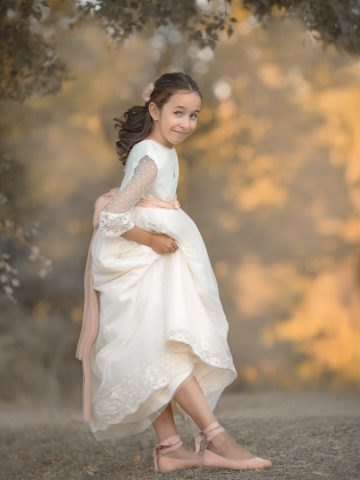 una foto de niña en vestido de primera comunión con lazo rosa y bailarinas rosa