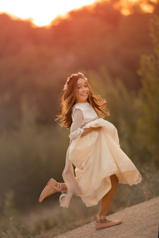 una Fotografía de niña feliz en su vestido de primera comunión al atardecer en el campo